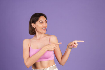 Fototapeta premium Young brunette in top isolated on purple background fit and pretty happy excited point right with index finger