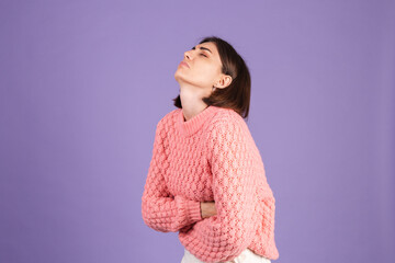 Young brunette in pink sweater isolated on purple background suffering stomach ache with painful...