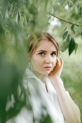 A young girl in a white shirt holds an earring with her hand and looks at the camera against the background of sheets