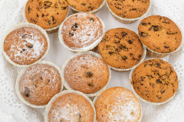 Muffins in paper cups on a white lace napkin. Cupcakes with dark filling and sprinkled with powdered sugar.