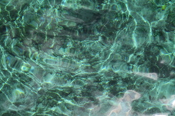 Blue and turquoise looking water surface in a cenote in mexico, the water is transparent, you can see some waves with bright light from the sun, perfect refresh for a sunny days
