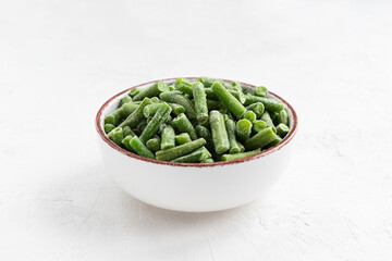 Frozen green beans in a bowl on a white table.