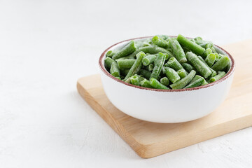 Frozen green beans in a bowl on a wooden board. Horizontal orientation, copy space.