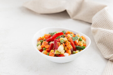 Mix of frozen vegetables in a bowl on a white table.