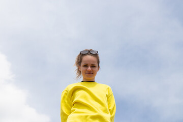 Attractive young girl wearing yellow long sleeve sweater standing outside under huge clouds.