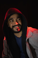 Retrato de hombre joven con barba sonriendo con una capucha en la cabeza y  fondo negro