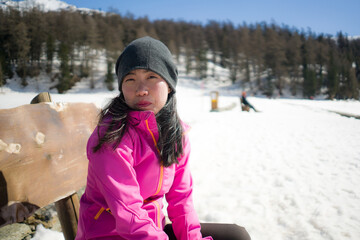 Fototapeta na wymiar freezing Winter holidays - young happy and beautiful Asian Korean woman on bench at frozen lake landscape surrounded by snow mountains enjoying Swiss Alps getaway
