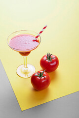 Glass with tomato juice and straw and tomatoes.