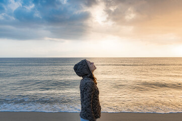 Side view casual woman with hood standing on the sea shore breathing and enjoying the fresh air.