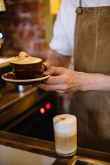 Cup of cappuccino into barista hands. Cup of latte coffee on the table.