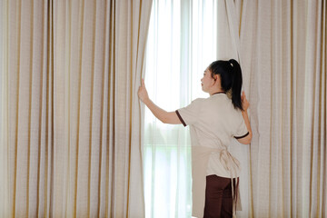 Young maid opening curtains in hotel room
