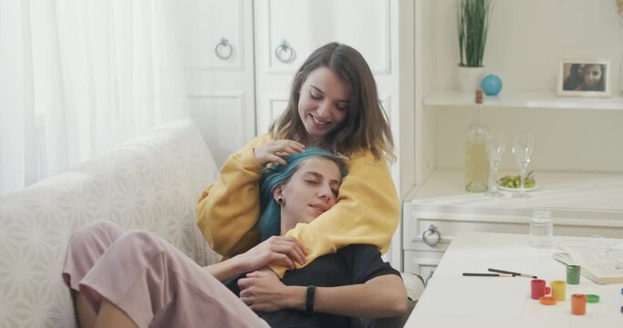 Two young lesbian lovers sharing a happy tender moment together as they embrace on a couch at home laughing and smiling