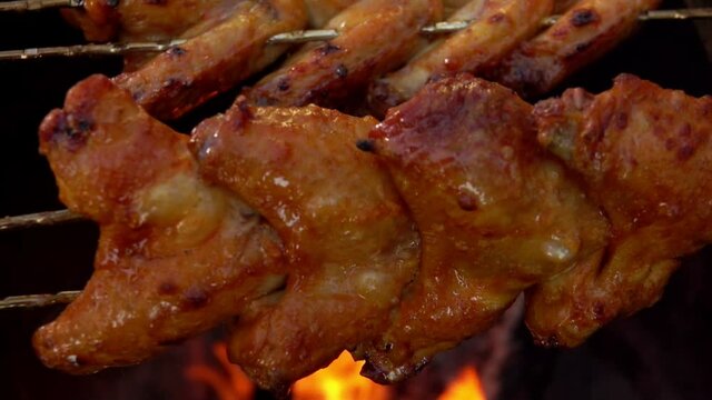 Close-up of delicious marinated chicken wings on the skewers rotated above the open fire outdoors