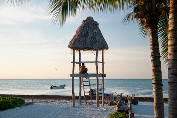 A wooden lifeguard hut on a tropical white sand beach on Holbox Island in Mexico. In the background, the sky, palm trees, and the Caribbean Sea.