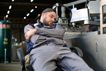 Tired factory worker sleeps at workplace near production line breaking rules