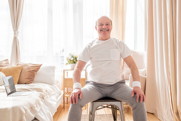 Elderly man wearing sport clothing sitting on chair ready for online yoga lesson