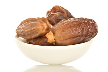Several dried organic light brown dates in a white saucer, close-up, isolated on white.