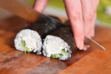 Chef cuts fresh cooked sushi roll with curd cheese and cucumber