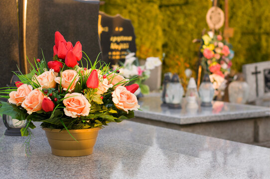 A tomb decorated with candles and flowers with cementary in the background.
