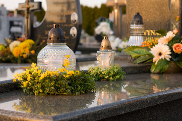 A tomb decorated with candles and flowers with cementary in the background. - obrazy, fototapety, plakaty