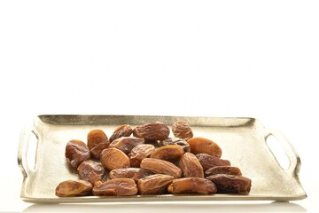 Several dried organic light brown dates on a metal tray, close-up isolated on white.