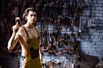 Obraz na płótnie Canvas Authentic handsome indian man in leathern apron hammer industry small business
