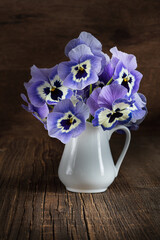  Beautiful pansies flowers in porcelain vase on dark wooden background.Rustic stil life photography.