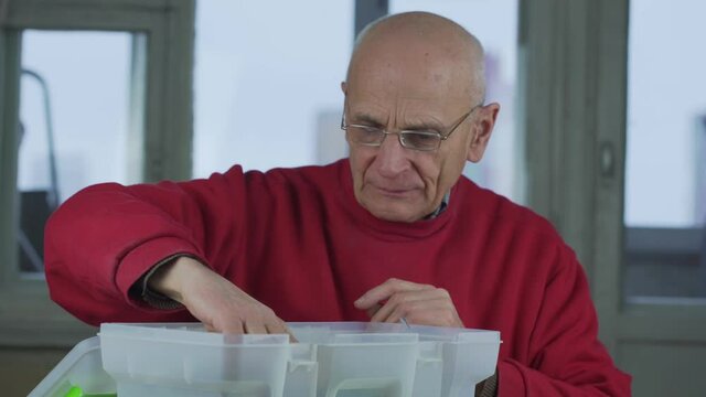 Senior joiner in glasses opens toolbox and takes of screwdriver and wrench
