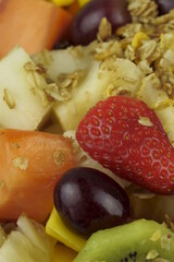 Fruit salad with chestnuts and granola in a bowl. Multicolored ripe fruits. Pineapple, mango, grape, strawberry, papaya, melon, banana and kiwi..