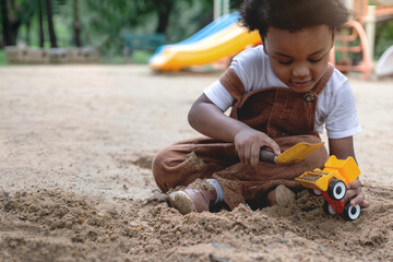 Dark-skinned child boy enjoy playing with toy cars and sand at playground