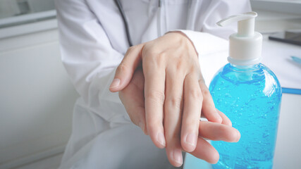 female doctor in a hospital waring white uniform is rubbing in palm with sanitizer alcohol gel...