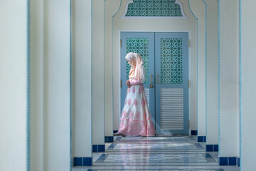 Fototapeta premium Beautiful Muslim woman in traditional clothing walks in the aisle of the mosque, covering her face with a scarf