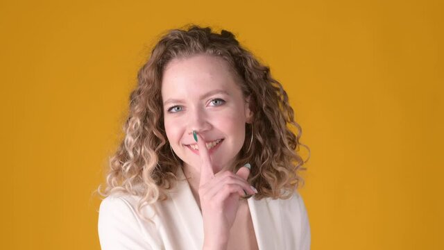 Women's secret. Young attractive blonde girl with curly hair smiling and holding finger on lips making silence gesture