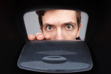 Man looking in plastic box with door. Close-up shot of shocked young man with round eyes.