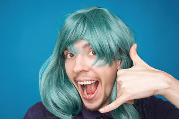 Funny portrait of a man with happy emotion on his face in the studio on blue background. Man wearing wig. Green hair