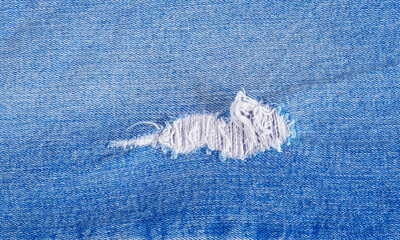 Tear of denim texture with a hole and threads showing.