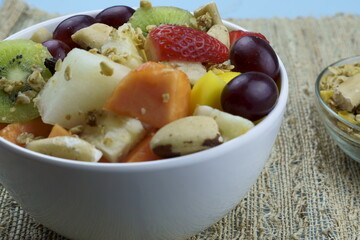 Fruit salad with chestnuts and granola in a bowl. Multicolored ripe fruits. Pineapple, mango, grape, strawberry, papaya, melon, banana and kiwi..