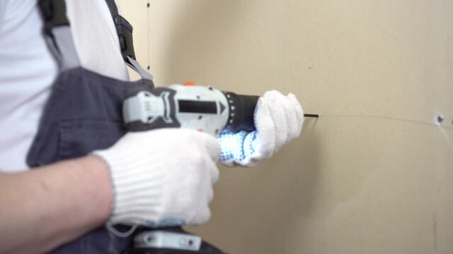 The builder screws the gypsum board with a self-tapping screw using a screwdriver on the wall closeup.