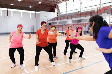 young girl sports monitor in sports center giving collective classes to older women for maintenance