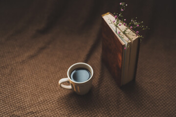 A book with flowers and cup of coffee on dark background top view