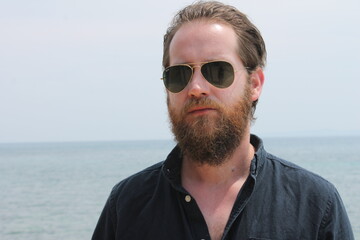 portrait of attractive man 30s with beard ocean sea behind him on sunny day 