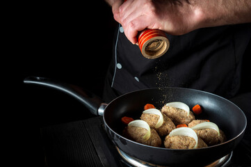 Cooking cutlets on grill pan by chef hands on black background for copy space text restaurant menu. The chef adds pepper