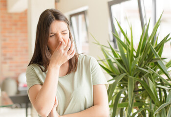 pretty woman feeling disgusted, holding nose to avoid smelling a foul and unpleasant stench