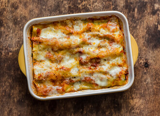 Fresh cannelloni pasta with spinach and ricotta baked with mozzarella cheese in a baking dish on a wooden background, top view