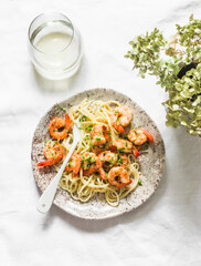 Delicious pasta. Spaghetti with garlic parsley shrimp and a glass of white wine on a light background, top view