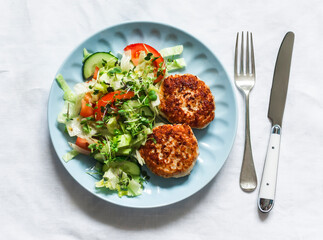 Chicken burgers and fresh iceberg, tomatoes, cucumber salad on a light background, top view