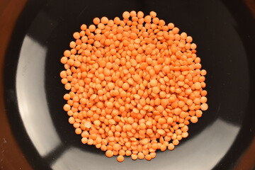 Red organic, uncooked lentils in a black dish, close-up, top view.