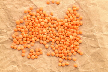 Red organic, uncooked lentils on craft paper, close-up, top view.