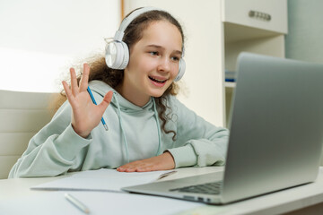 Start of on-line lesson. Smiling female student in headphones greets and waves his hand before the...