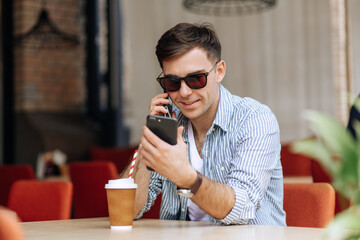 Handsome brunet man sitting in a cafe and smiling, talking on the phone and looking at another